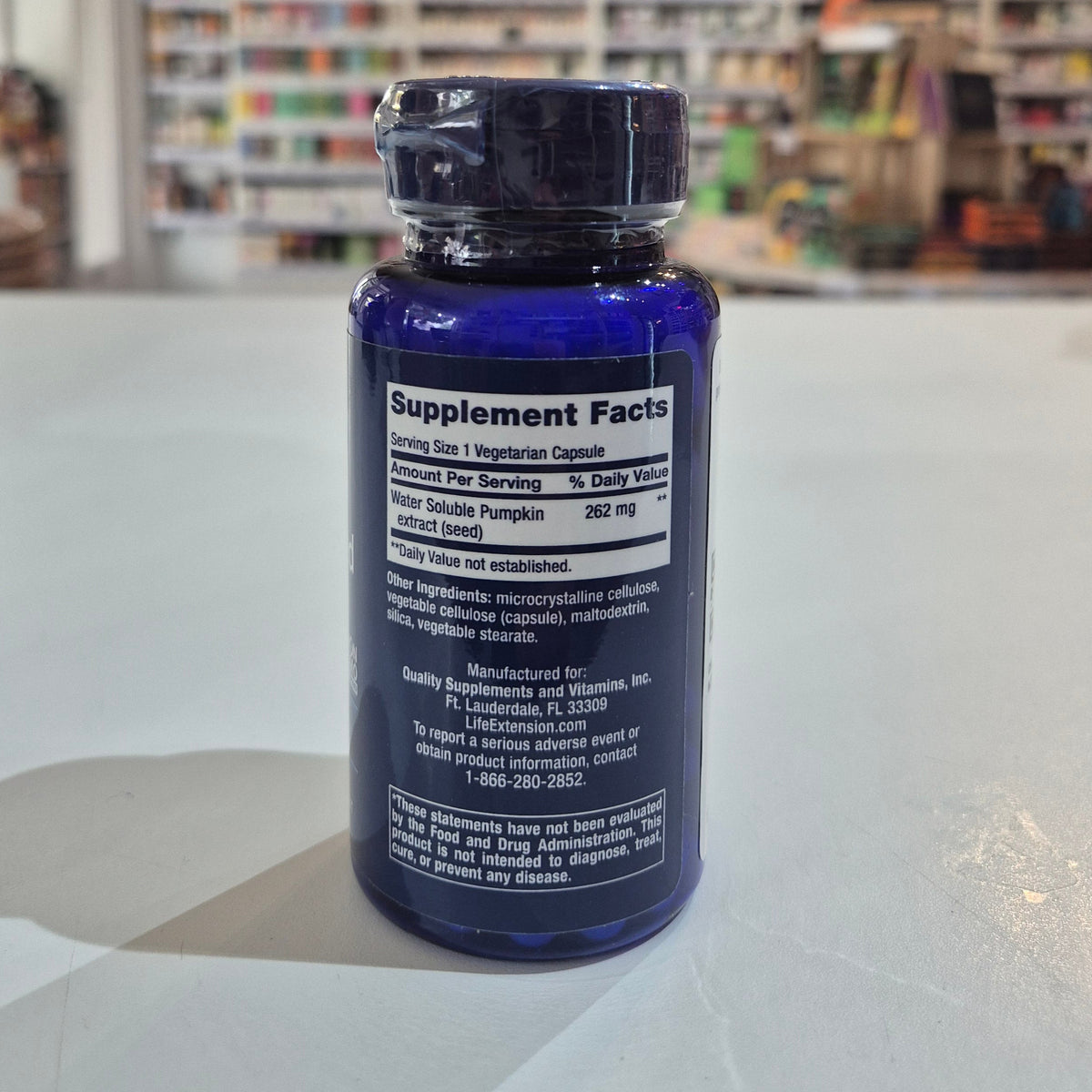 Blue supplement bottle with label on a white surface, blurred store background