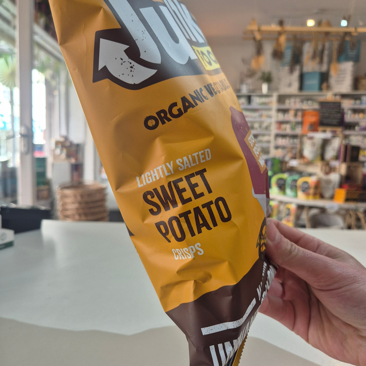 Hand holding a package of organic sweet potato chips in a store setting