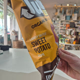 Hand holding a package of organic sweet potato chips in a store setting