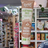 A hand holding a tube of Tartex mushroom pate in a retail store setting with shelves of products in the background.