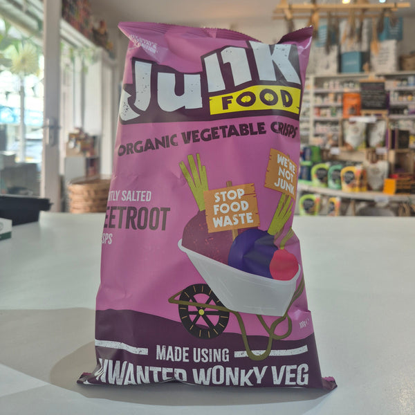 Purple bag of 'Junk Food' organic vegetable crisps on a white surface with a store background.