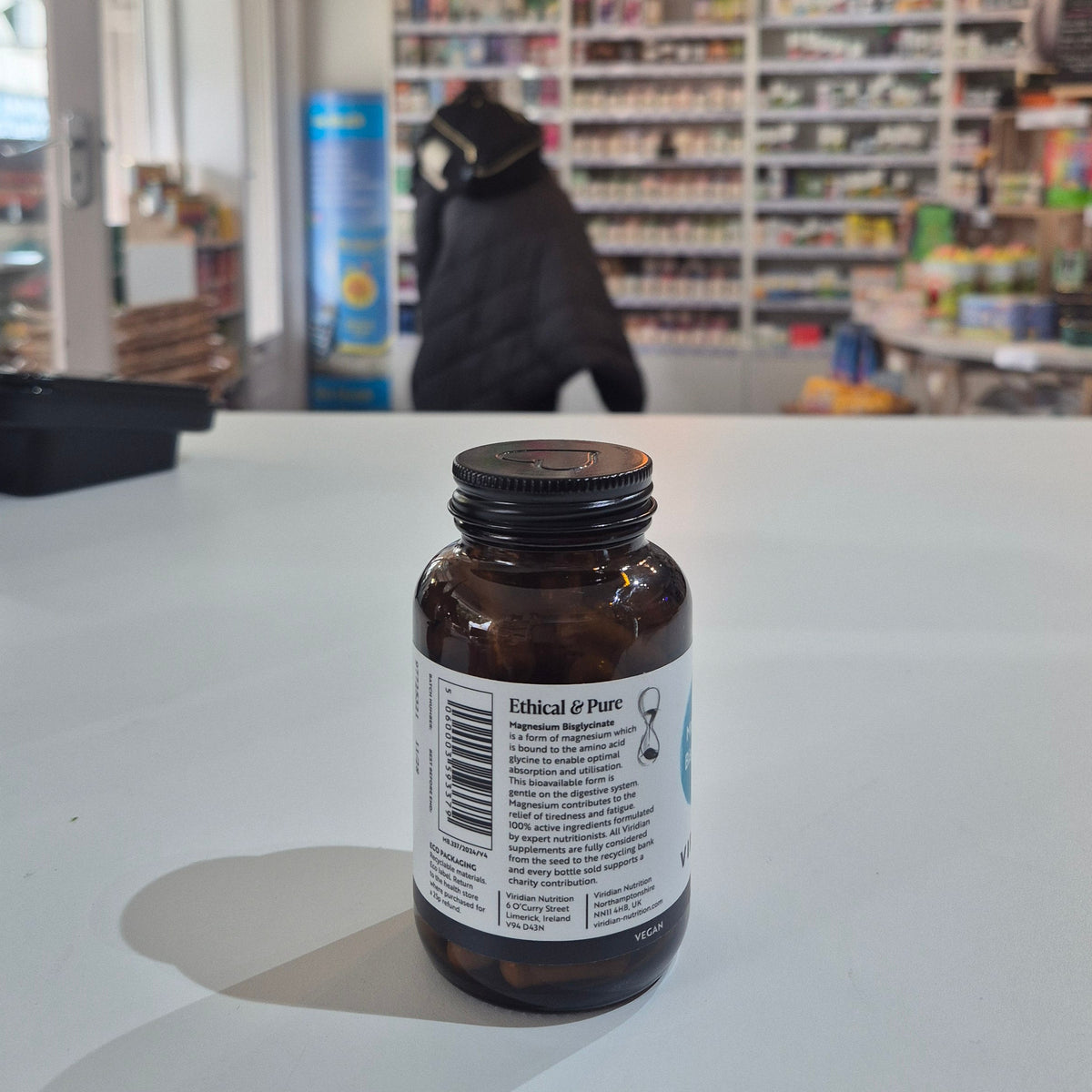 Brown bottle with label on a white surface, blurred background of a store interior.