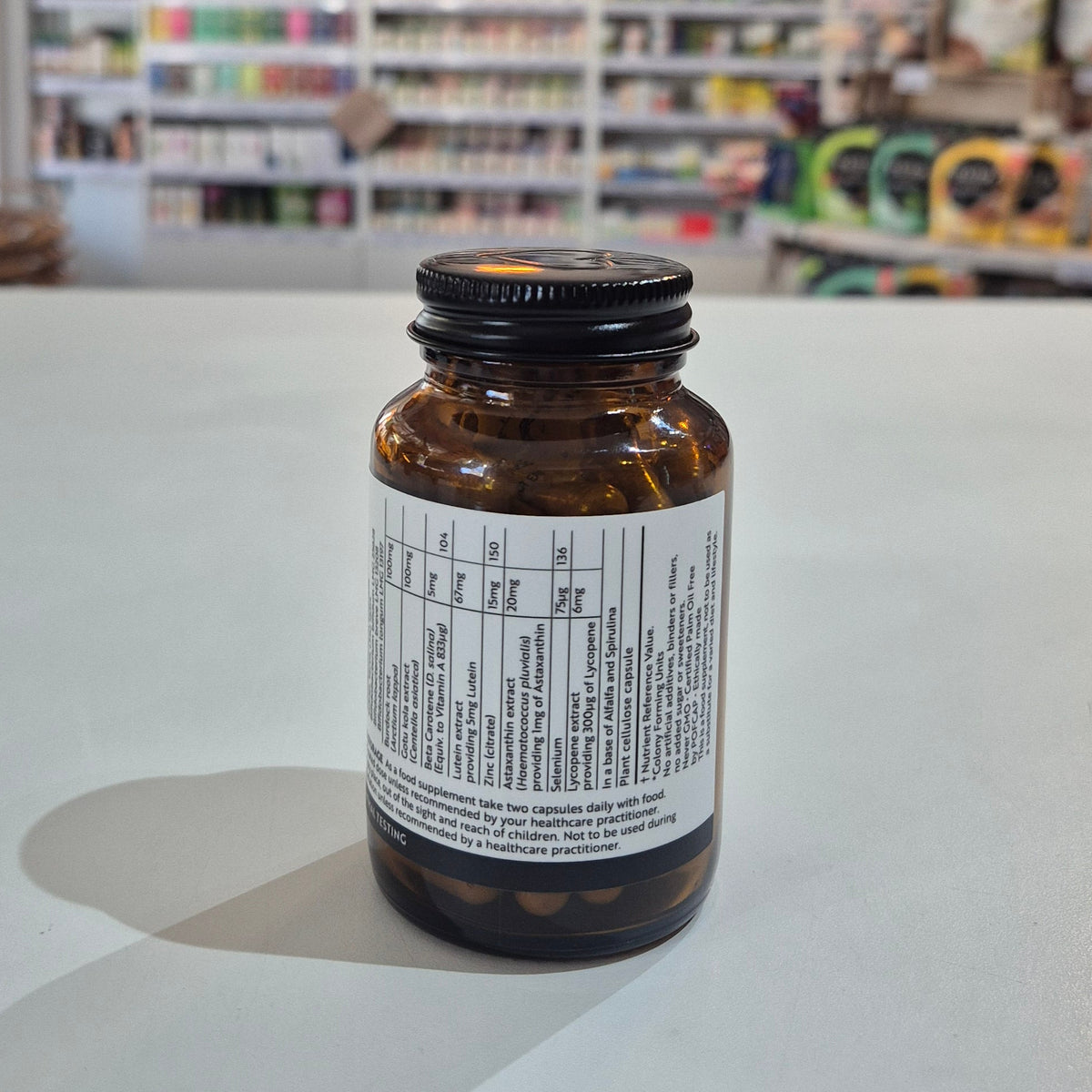 Brown supplement bottle with label on a white surface, blurred store shelves in the background