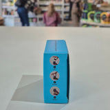 Fussy compostable deodorant refill packaging with a store in the background. Blue box with icons and text on a light gray surface, blurred background of people and products.