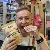 Man eating plantain chips from a 'Purely' package in a store setting