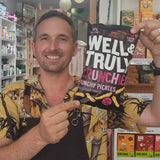 A bag of Well & Truly Crunchies Crunchy Pickles snack chips is being held by a man. 