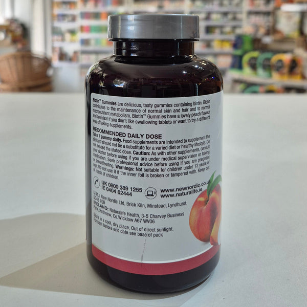 Bottle of New Nordic Biotin Gummies with peach flavor label on a counter. Supplement bottle with label on a white surface, blurred store background