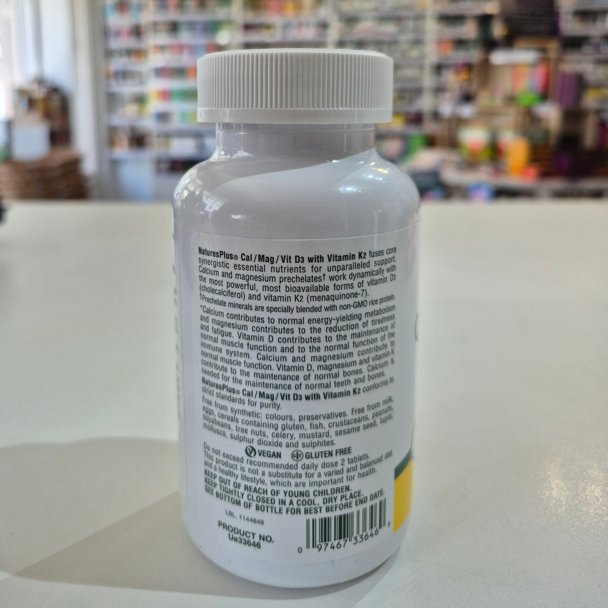 NaturesPlus Cal/Mag/Vit D3 supplement bottle on a table with a blurred store background. Supplement bottle with label on a blurred store background