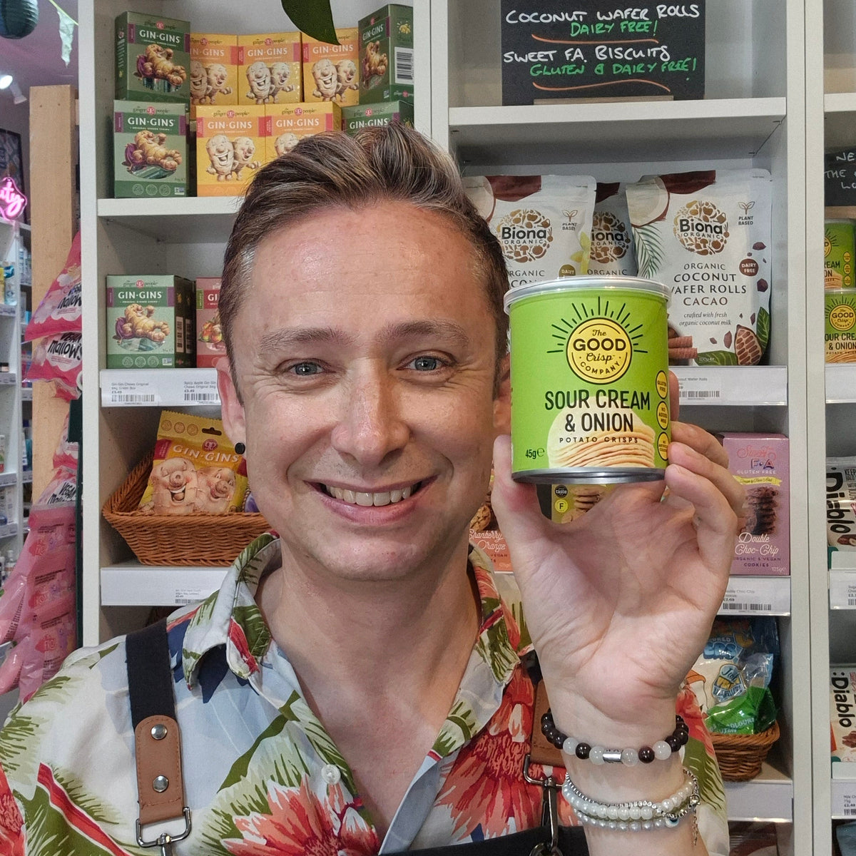 Man holding a can of 'The Good Crisp Company sour cream & onion dip in front of shelves with various food products.