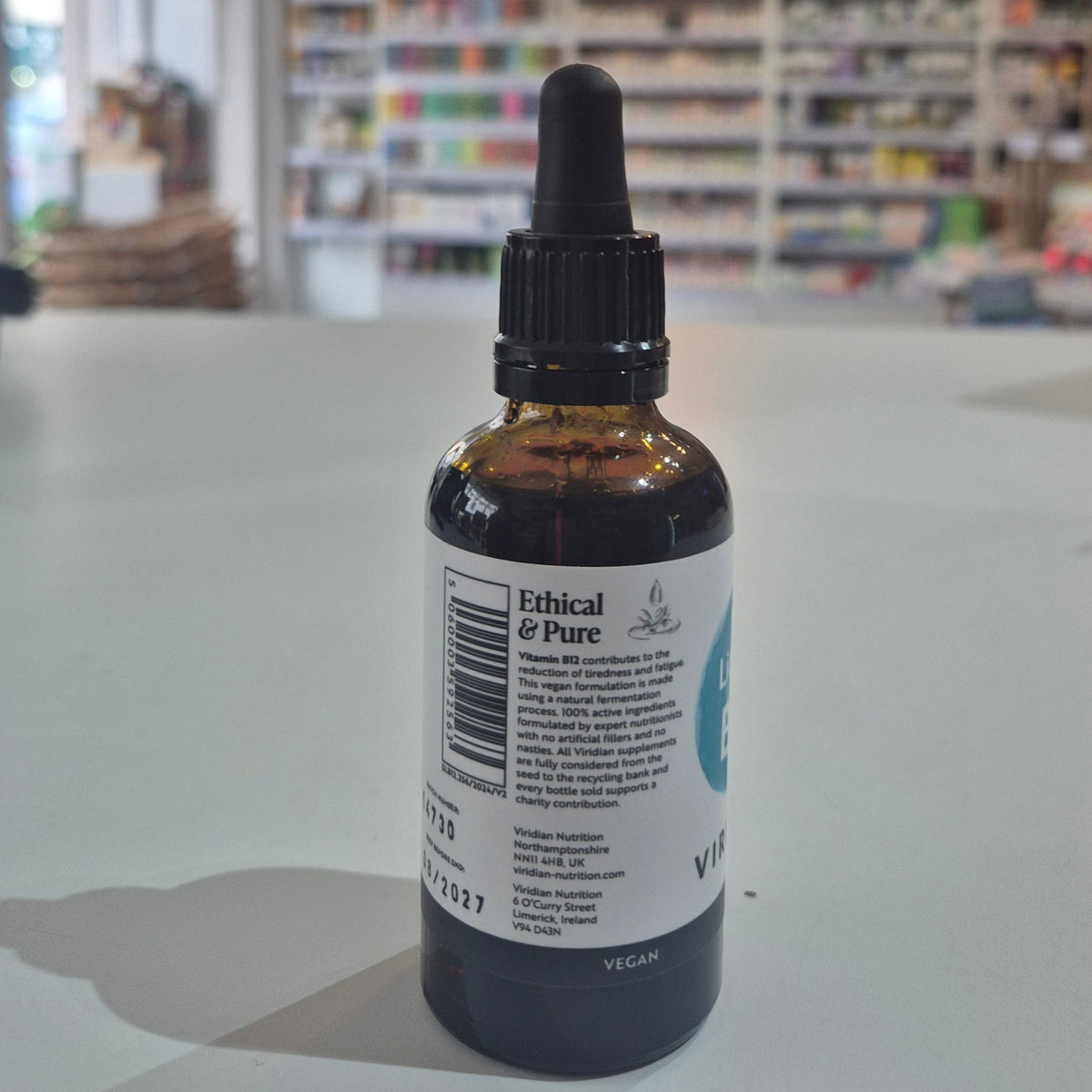 Bottle of Viridian Liquid B12 on a table with a blurred store background. Bottle labeled 'Ethical & Pure' on a surface with a blurred background