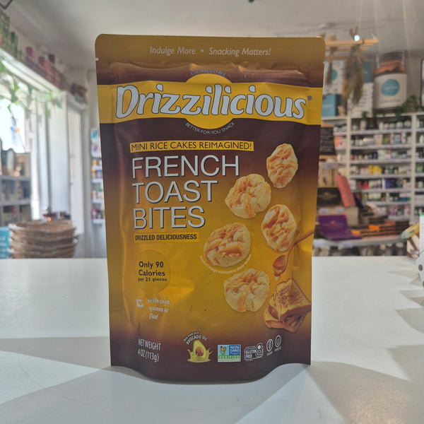 A bag of Drizzilicious French Toast Bites standing on a white counter in a retail store setting. The packaging is brown and gold with white text and images of the baked snack pieces.