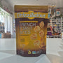 A bag of Drizzilicious French Toast Bites standing on a white counter in a retail store setting. The packaging is brown and gold with white text and images of the baked snack pieces.