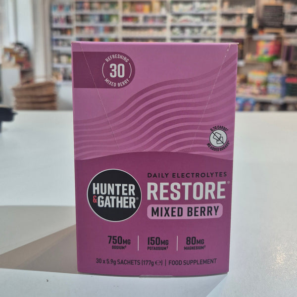 Purple Hunter & Gather supplement package with 'Restore' and 'Mixed Berry' text on a blurred indoor background. 