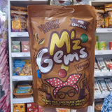 A bag of Mummy Meegz Mz Gems Vegan Milk Chocolate wrapped in a sweet crunchy shell, held up in front of a store shelf.