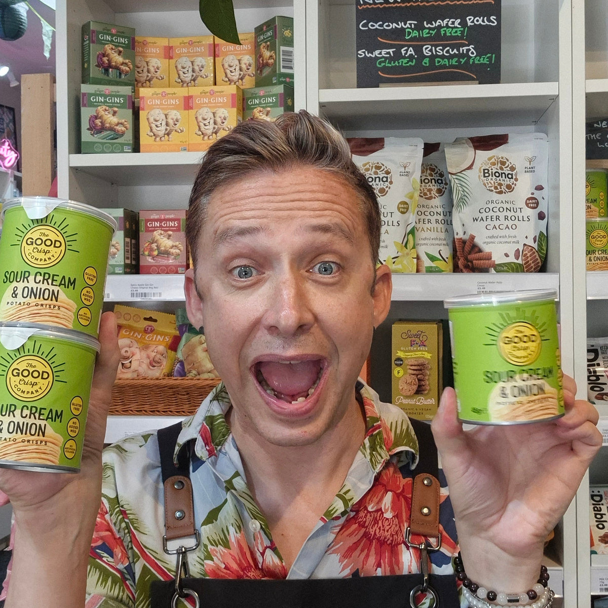 Person holding three containers of The Good Crisps Company Sour Cream & Onion chips in front of a store shelf.