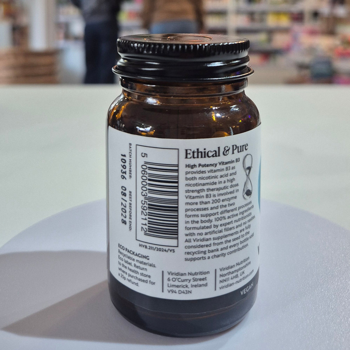 Vitamin B3 supplement bottle with 'Viridian' label on a blurred store background. Brown glass bottle with a label on a white surface, blurred background