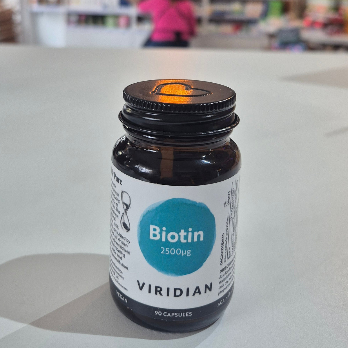 Bottle of Viridian Biotin on a white surface with a blurred store interior in the background.