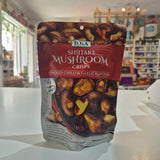 A bag of D.J & A Shiitake Mushroom Crisps in smoked chili & garlic flavour, placed on a white counter in a blurred retail store setting.