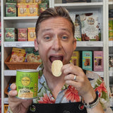 Man holding a can of 'Sour Cream & Onion' potato crisps from The Good Crisp Company in front of a shelf with various snacks.
