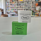 Fussy compostable deodorant refill container and packaging on a counter with a store background.