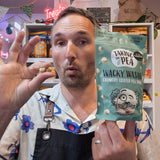 A man wearing a floral shirt and black apron holds up a bag of 'Taking the Pea' Wacky Wasabi Crunchy Coated Pea Snacks, making a gesture with his other hand while showing the product packaging in a retail setting.