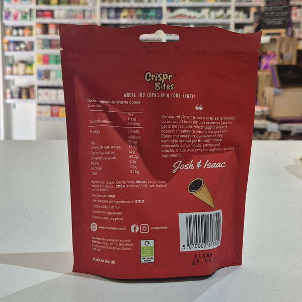 A person holds a red bag of Crispr Bites Dark Chocolate Filled Waffle Cones in a brightly lit shop interior with the ingredients showing. 