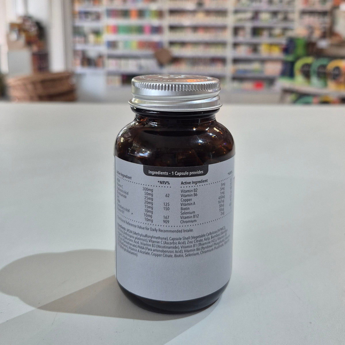 Supplement bottle labeled 'balanced' for hair, skin, and nails on a table with a blurred store background. Brown supplement bottle with white label on a light surface, blurred store background