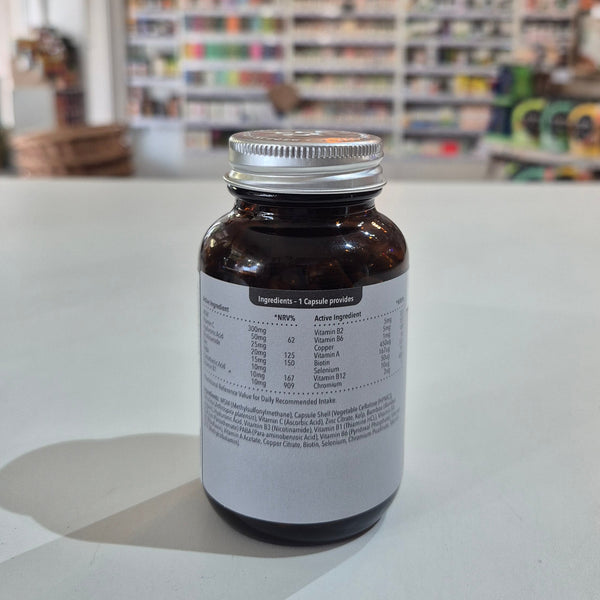 Supplement bottle labeled 'balanced' for hair, skin, and nails on a table with a blurred store background. Brown supplement bottle with white label on a light surface, blurred store background