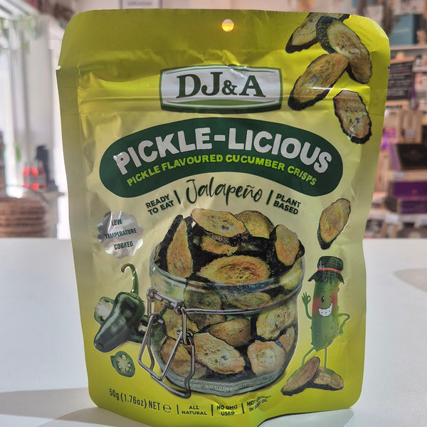 A bag of DJ&A Pickle-Licious Jalapeno pickle-flavoured cucumber chips on a white surface, with a blurred indoor shop background.