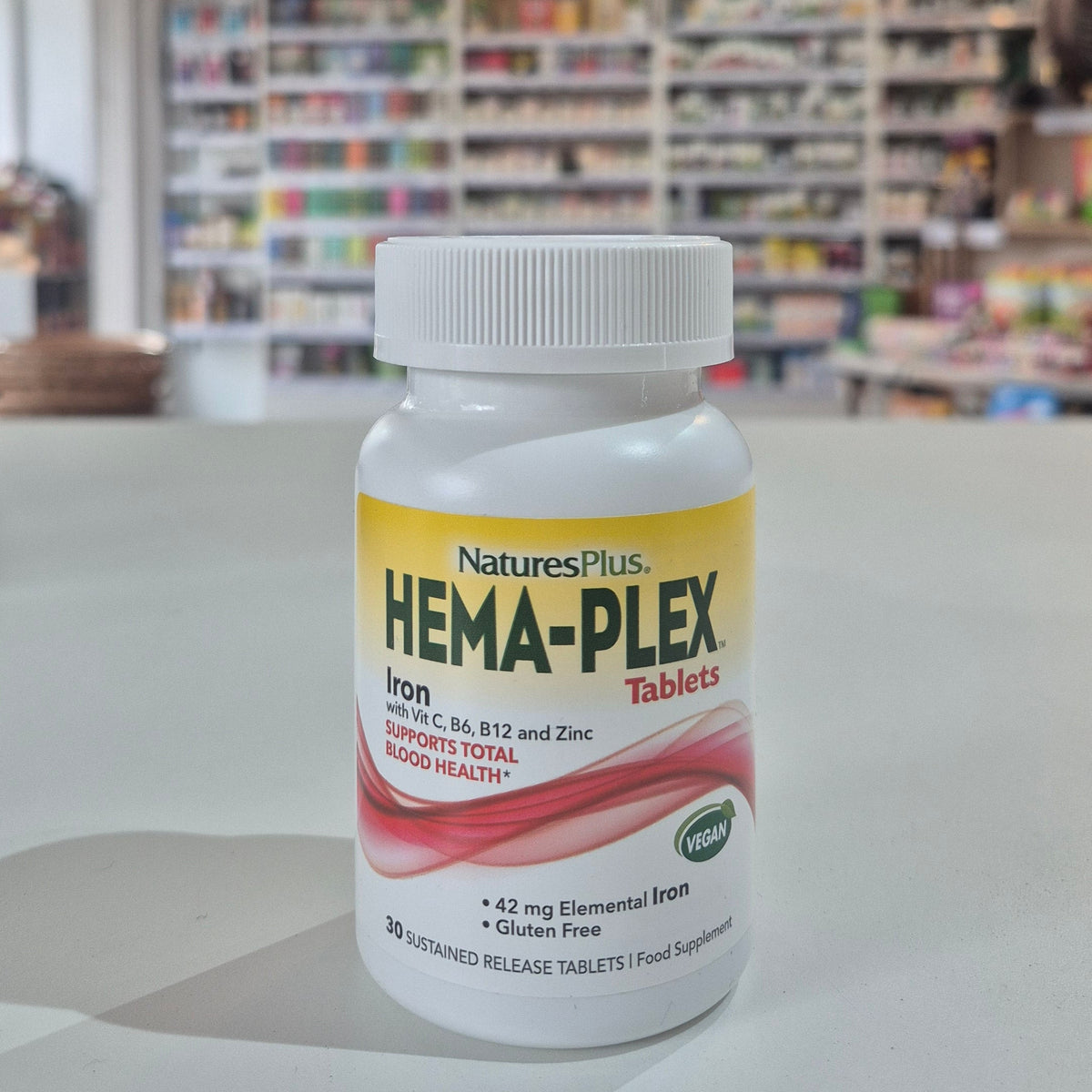 Bottle of Natures Plus Hema-Plex Tablets 42mg Elemental Iron, 30 capsules on a white surface with a blurred indoor background.