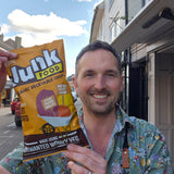 Man holding a packet of 'Junk Food' organic vegetable crisps on a street.