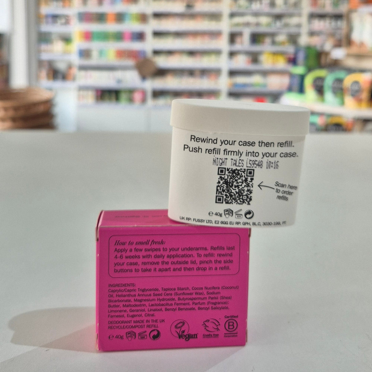 Pink deodorant refill box labeled 'fussy' on a gray surface with a blurred store background.