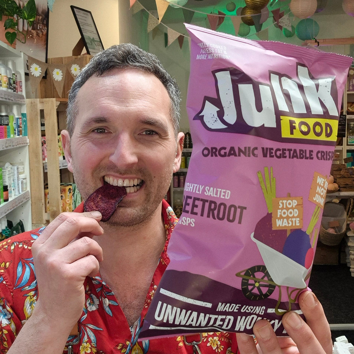 Man holding a bag of 'Junk Food' organic vegetable crisps and eating one.