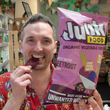Man holding a bag of 'Junk Food' organic vegetable crisps and eating one.