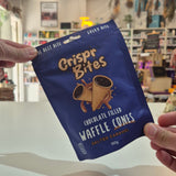 A person holds up a blue bag of Crispr Bites Chocolate Filled Waffle Cones in a shop setting.