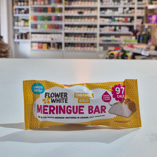 A packaged meringue bar snack placed on a white counter in a blurred shop interior with shelves and hanging decor in the background.