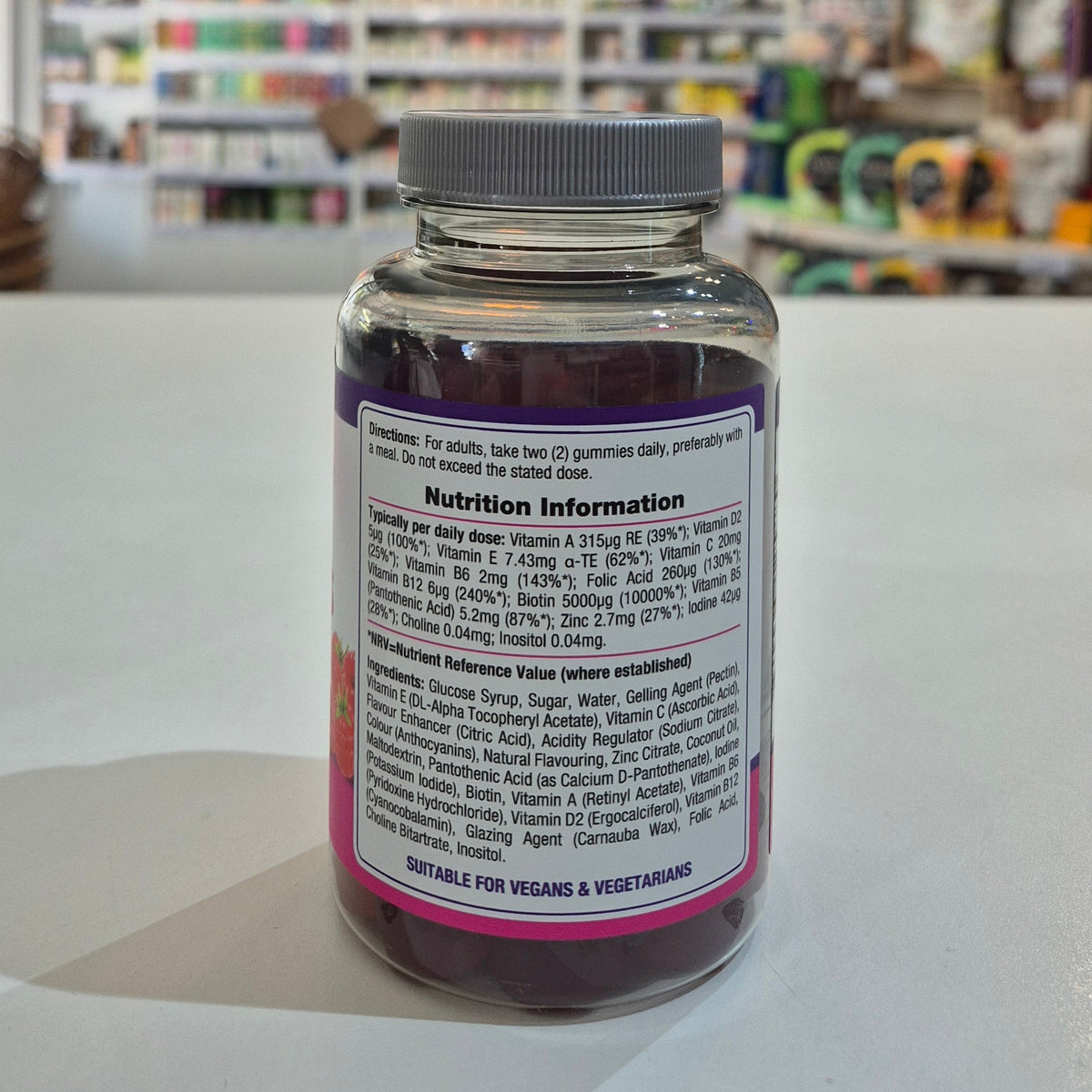 Nature's Truth Hair, Skin & Nails Gummies bottle on a white surface with a blurred store background. Supplement bottle with nutrition label on a white surface in a store setting