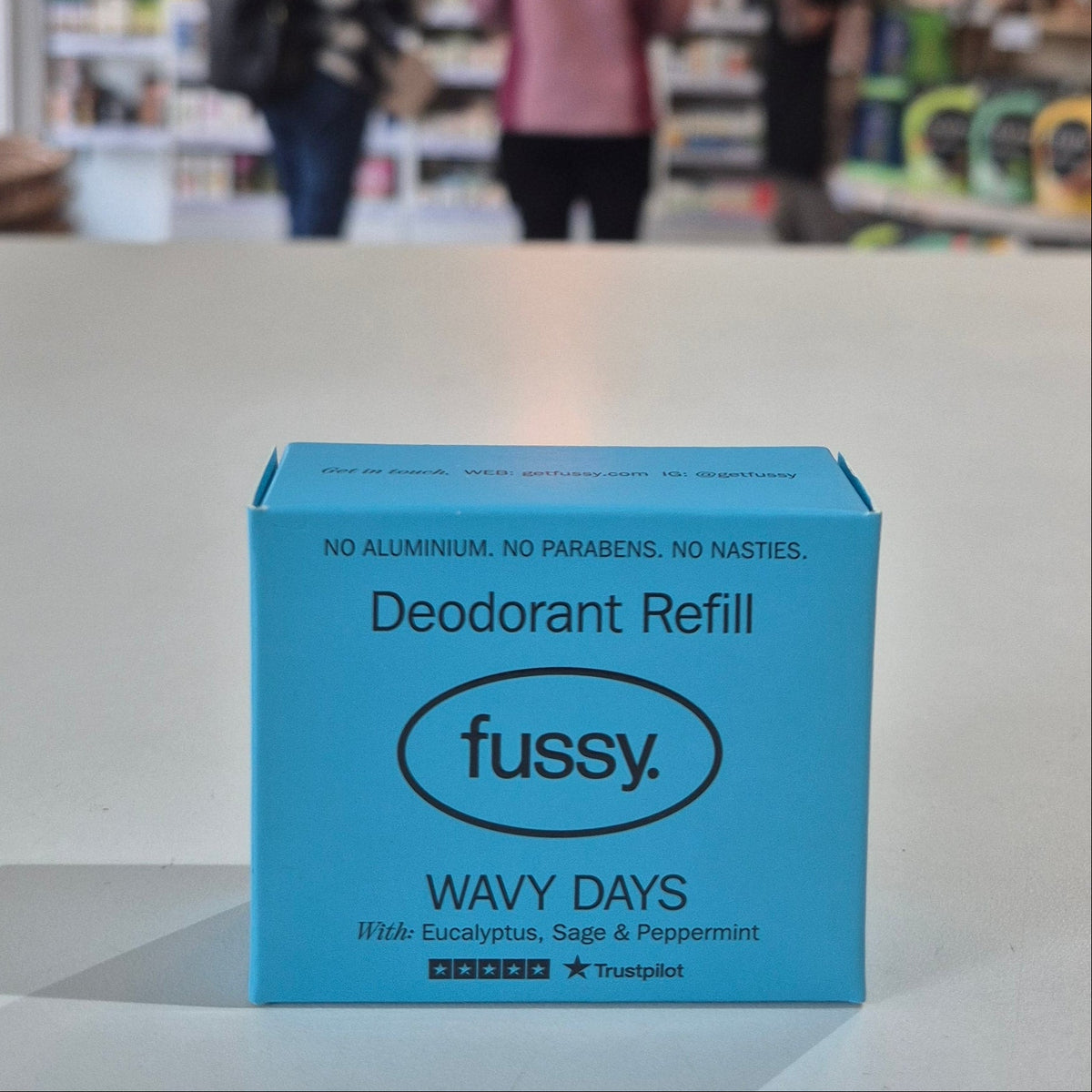 Blue 'fussy.' deodorant refill box on a surface with a blurred store background