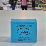 Blue 'fussy.' deodorant refill box on a surface with a blurred store background