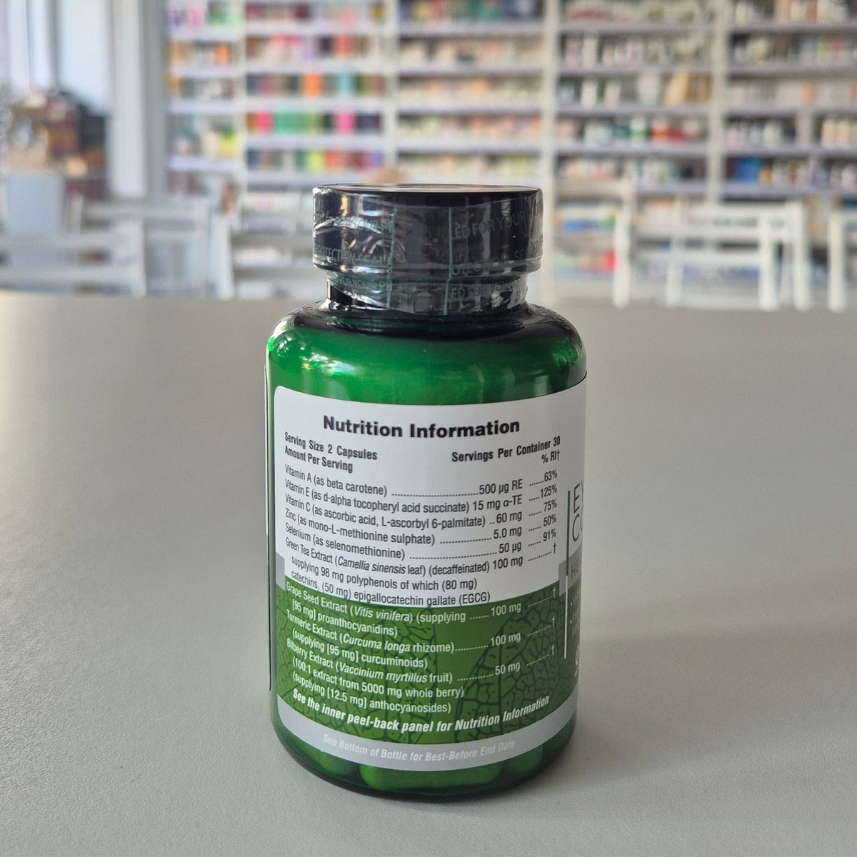 Green supplement bottle with nutrition information label on a gray surface, blurred library background