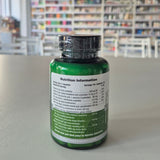 Green supplement bottle with nutrition information label on a gray surface, blurred library background