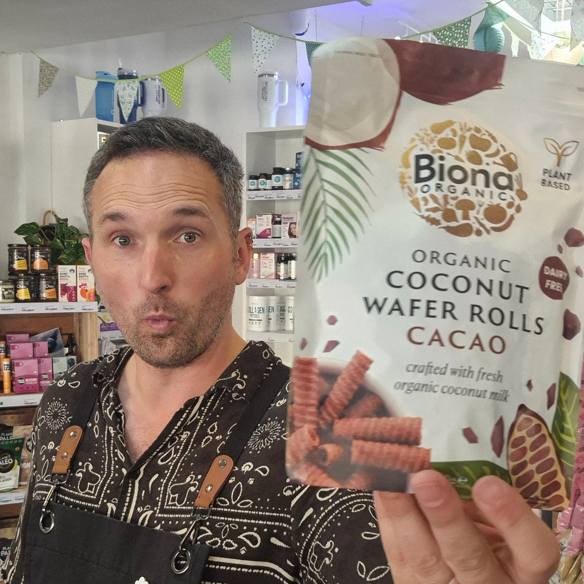 Man holding a package of Biona Organic Coconut Wafer Rolls Cacao in a store setting.