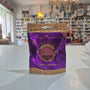 A purple and gold bag of Booja-Booja Chocolate Wonders Cookie Dough Organic, standing on a white countertop with a blurred shop interior in the background.