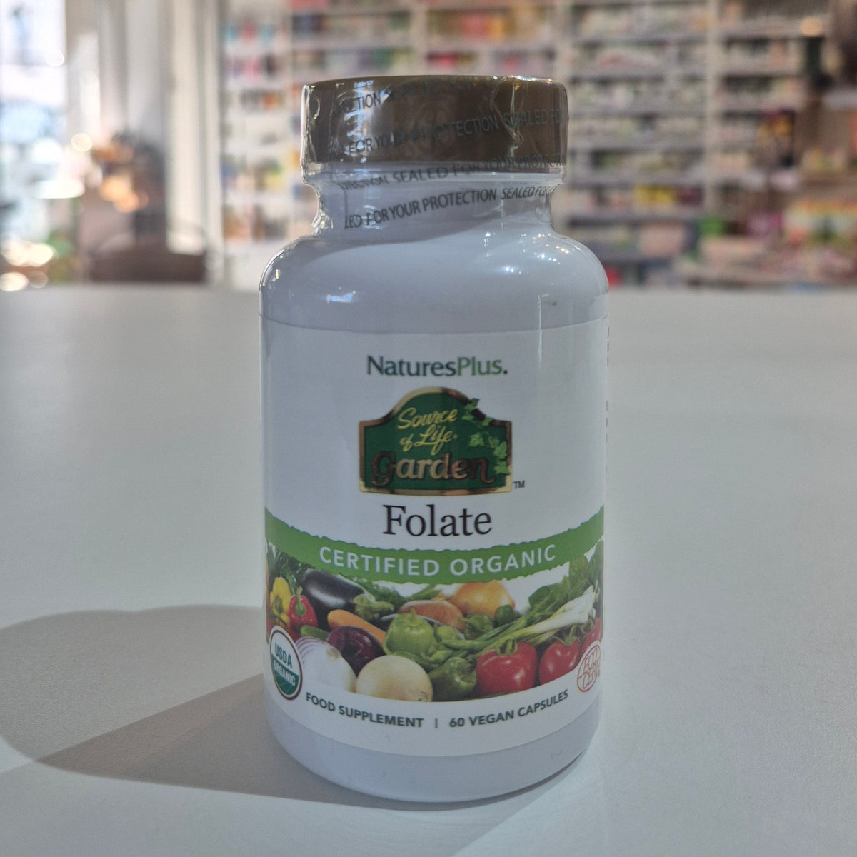 NaturesPlus Folate supplement bottle on a counter with a blurred store background