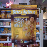 A person holds up a large bag of Drizzilicious French Toast Bites in a retail store aisle. The bag is predominantly golden yellow and dark brown with white and blue text, and images of the mini rice cakes and toast are printed on the front.