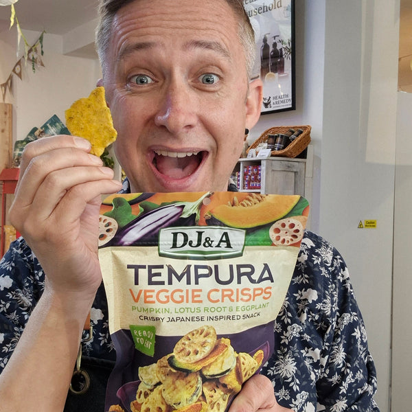 Person holding a bag of DJ&A Tempura Veggie Crisps in a kitchen setting