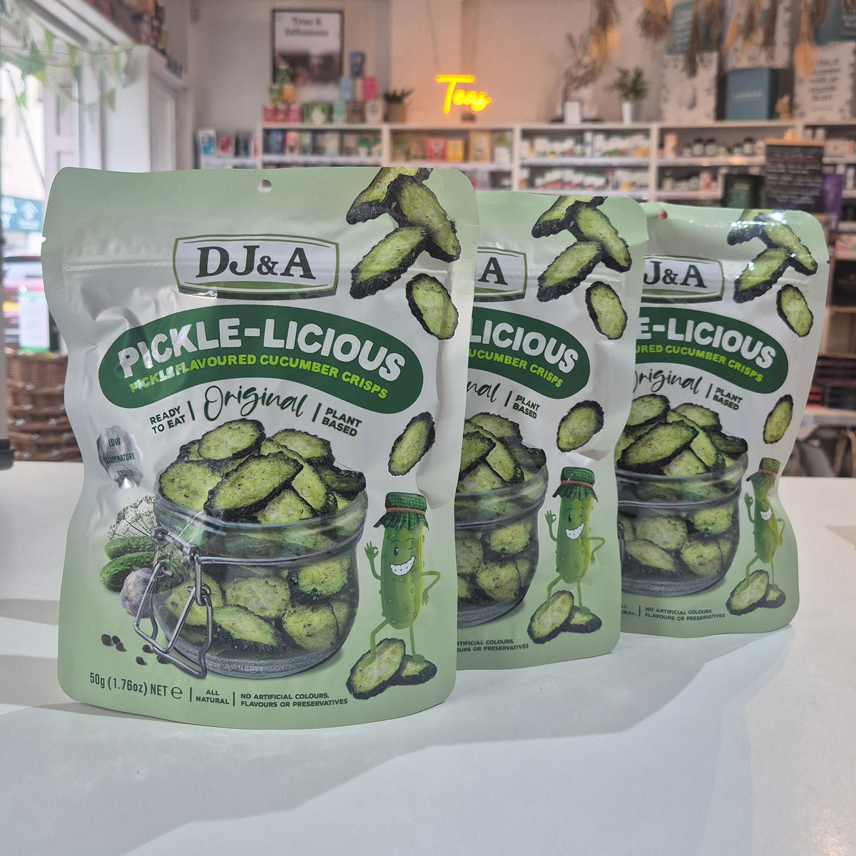 Three packages of D&A Pickle-Licious pickles on a white surface with a store interior in the background.