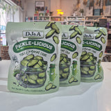 Three packages of D&A Pickle-Licious pickles on a white surface with a store interior in the background.