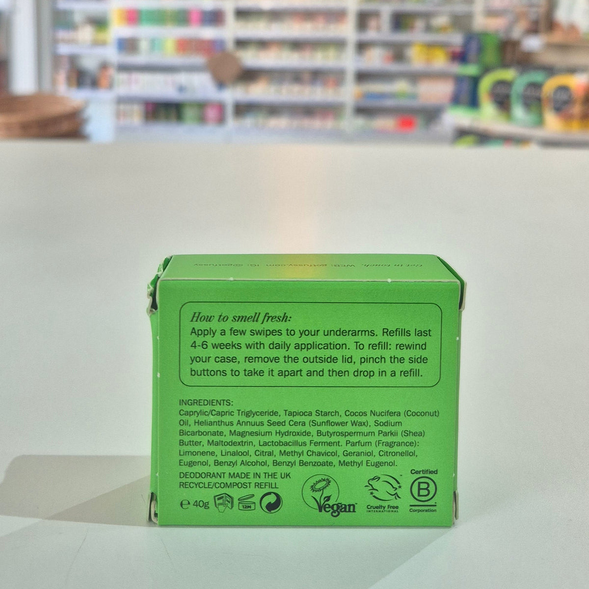 Fussy compostable deodorant refill container and packaging on a counter with a store background. Green box with text and logos on a white surface with a blurred background