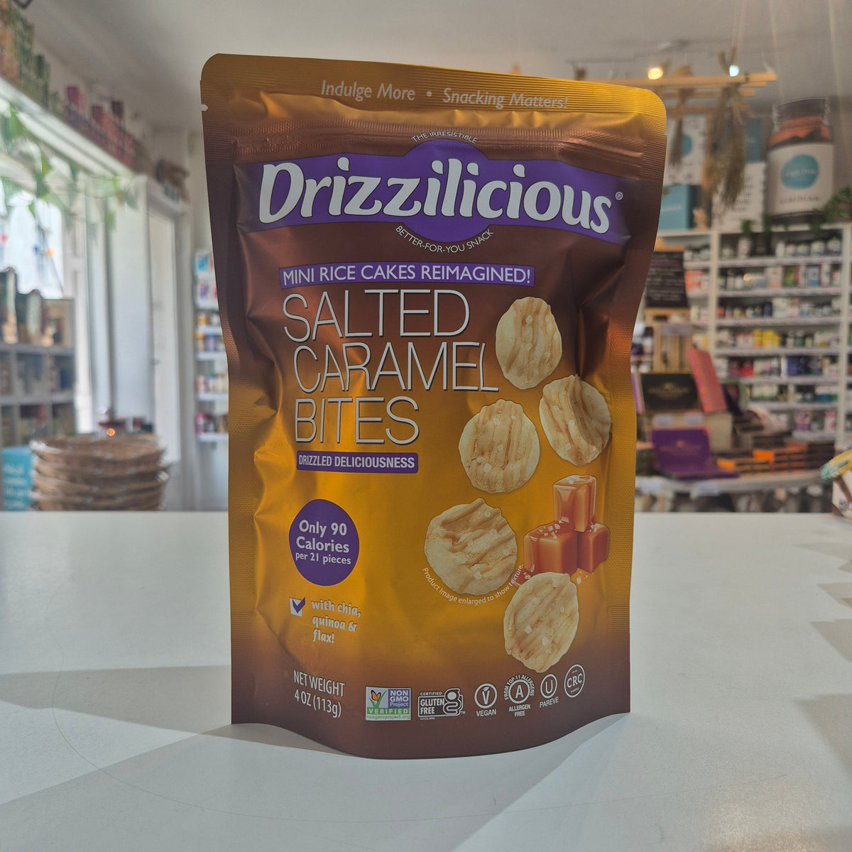 A bag of Drizzilicious Salted Caramel Bites mini rice cakes standing on a white countertop in a blurred retail store setting.